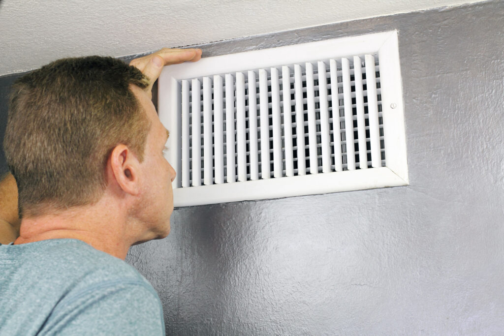 Mature man examining an outflow air vent grid and duct